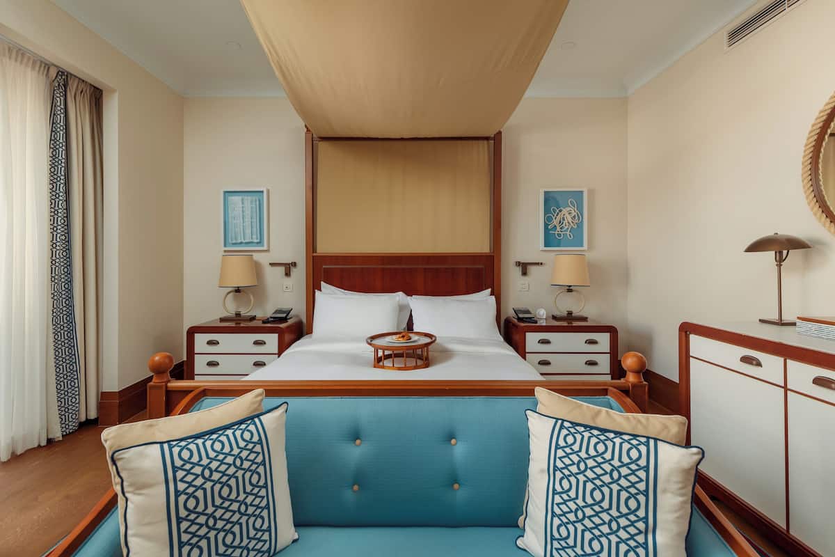 A hotel room with a large bed, two bedside tables with lamps, a blue sofa, and a wooden headboard.