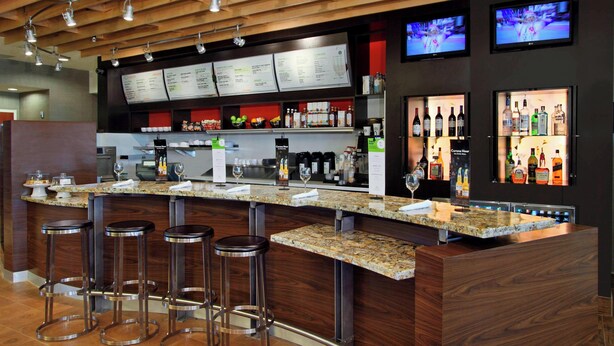 A bar area with a granite countertop, multiple stools, a menu board, and a selection of liquor bottles. - Courtyard by Marriott Victoria (Victoria)