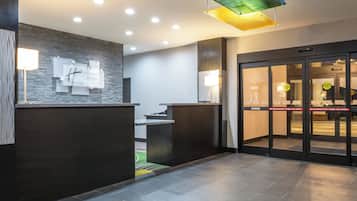 A hotel reception area with a modern design, including a reception desk, a wall-mounted sign, and a glass door with emergency instructions.