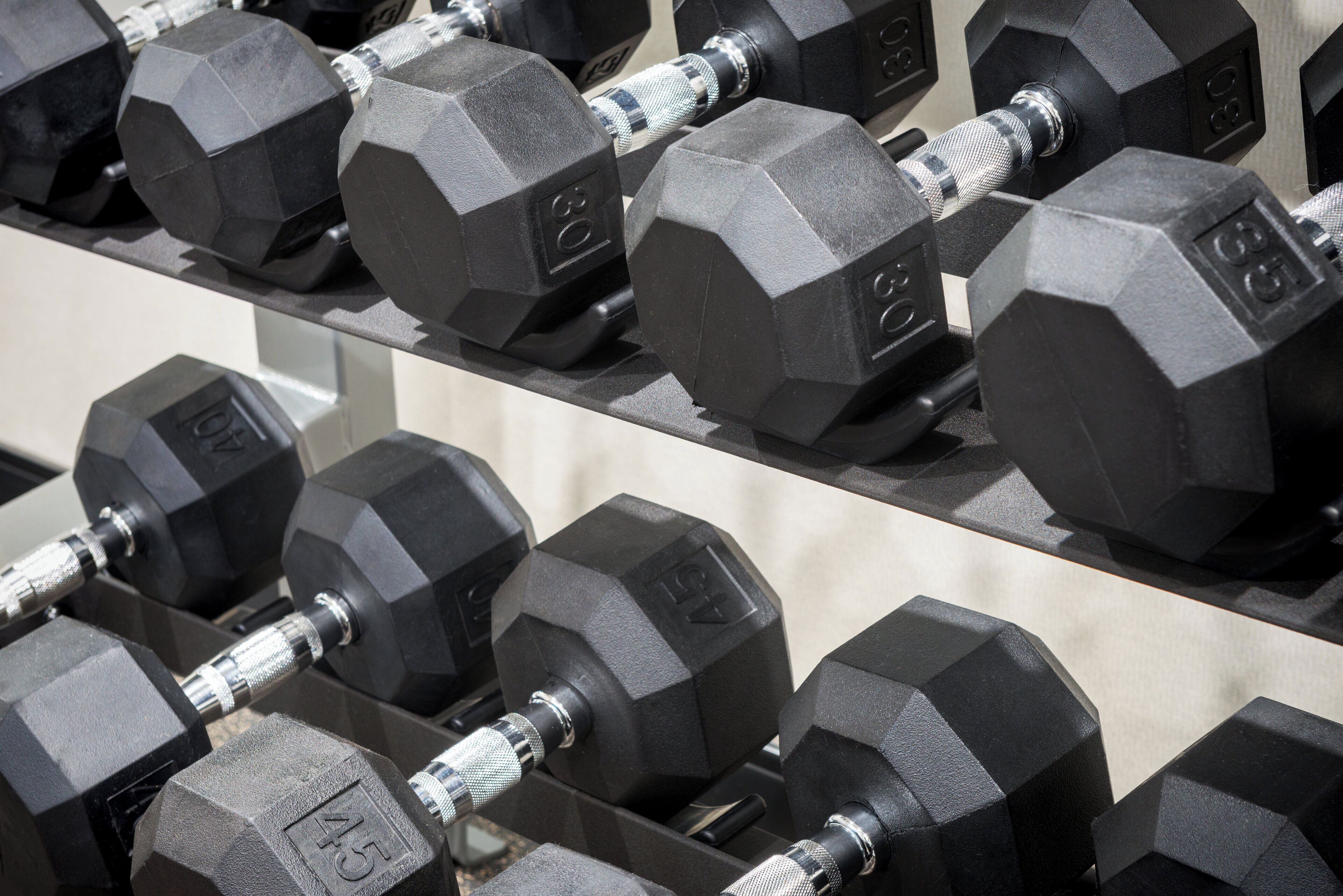 A rack of black hexagonal dumbbells with weight markings.