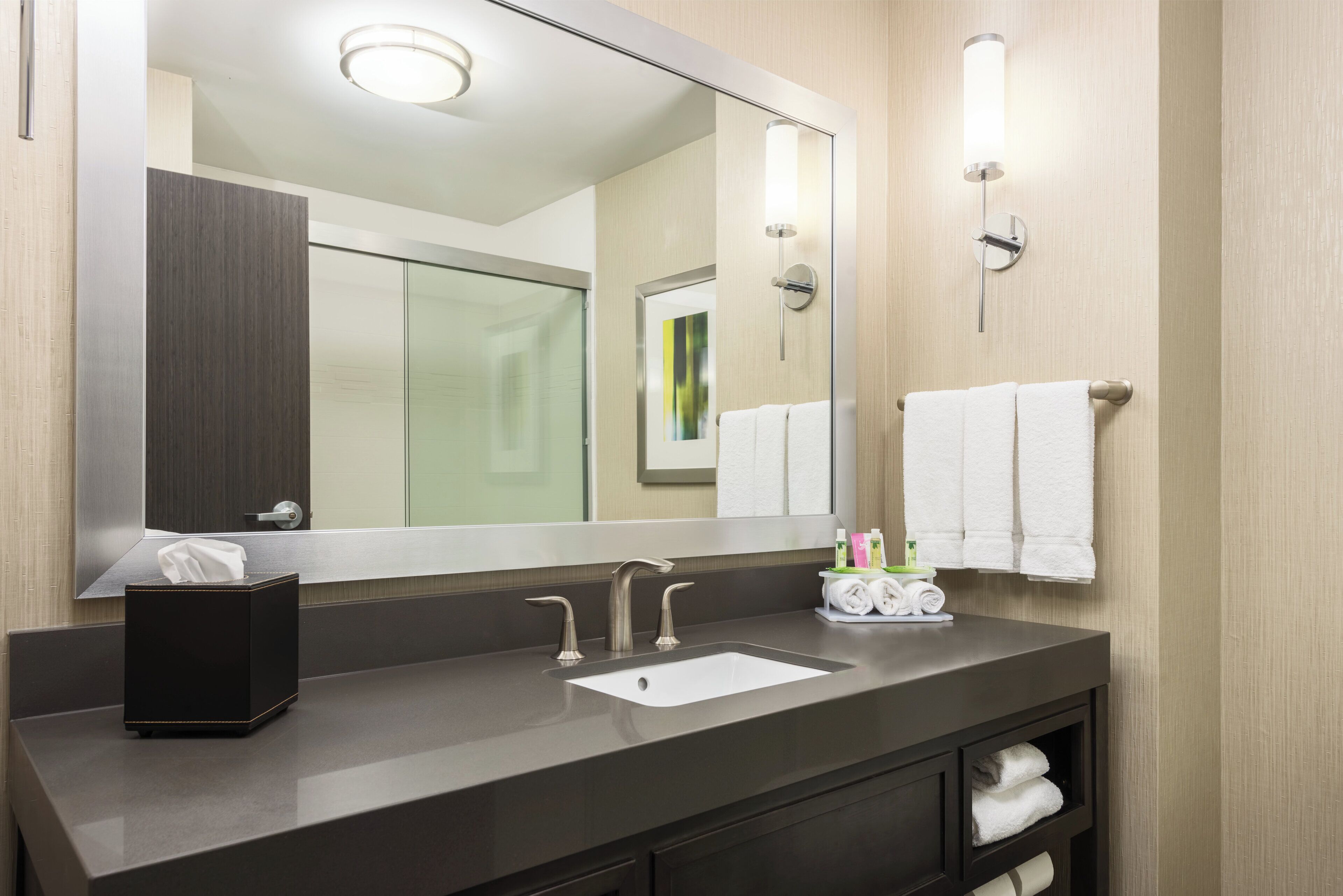 A modern bathroom with a large mirror, a sink, and a towel rack.