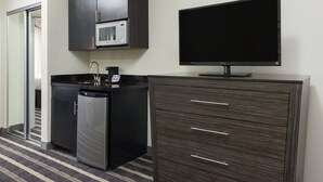 Una kitchenette compacta con microondas, pileta y lavavajillas, un televisor de pantalla plana y un mueble de madera oscura con cajones.