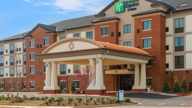 Un hotel Holiday Inn Express con fachada de ladrillo, un acceso cubierto y un jardín delantero ajardinado.
