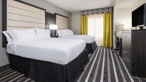 Habitación de hotel con dos camas, un escritorio, televisor y una ventana con cortinas amarillas.