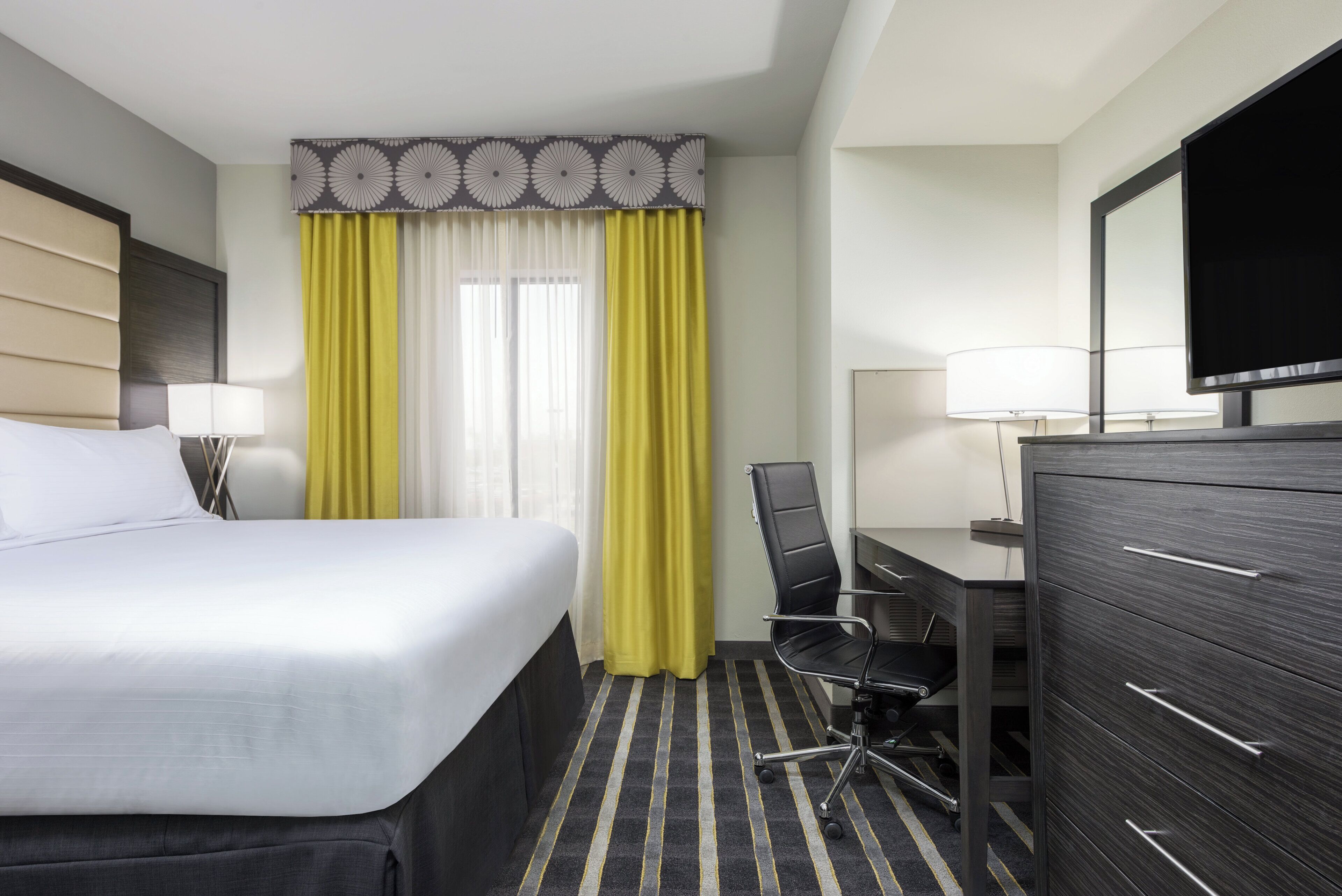 Une chambre d’hôtel comprenant un lit, un bureau, une chaise, une commode et un téléviseur.