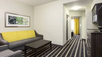 Habitación de hotel con sofá, mesa de centro, televisor y área de cocina con microondas.