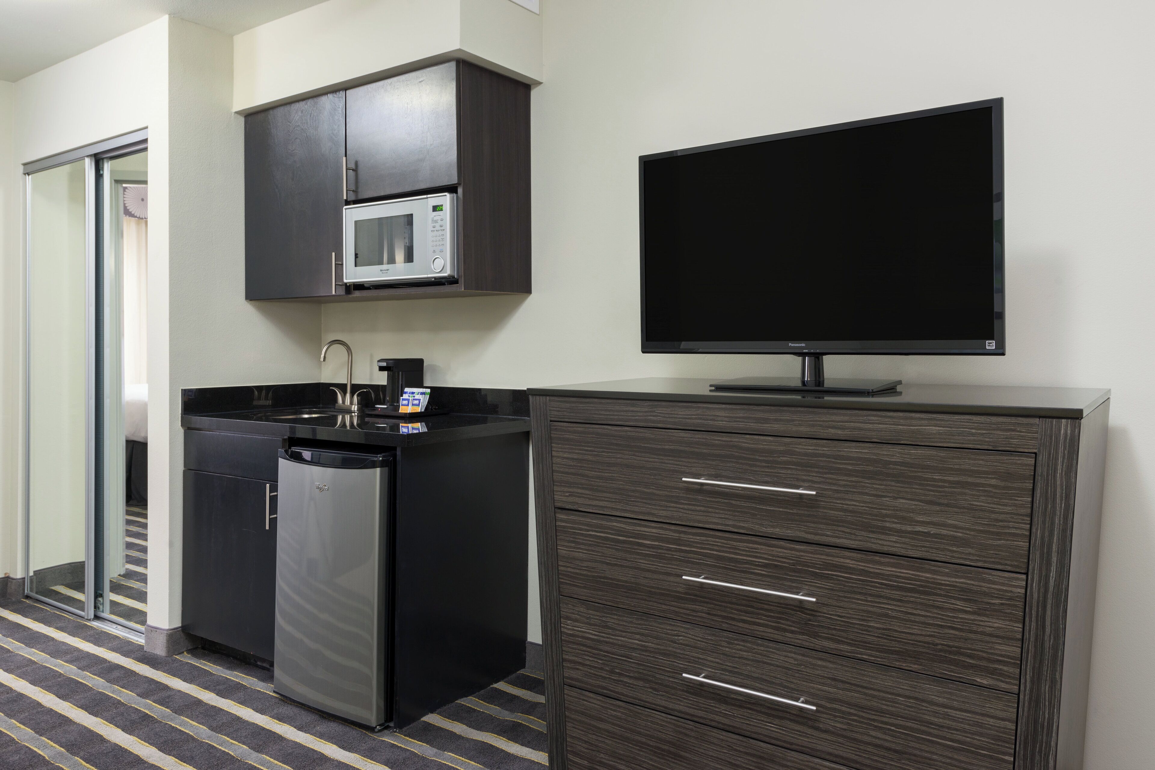 A compact kitchen with a microwave, dishwasher, and a flat-screen TV on a cabinet.