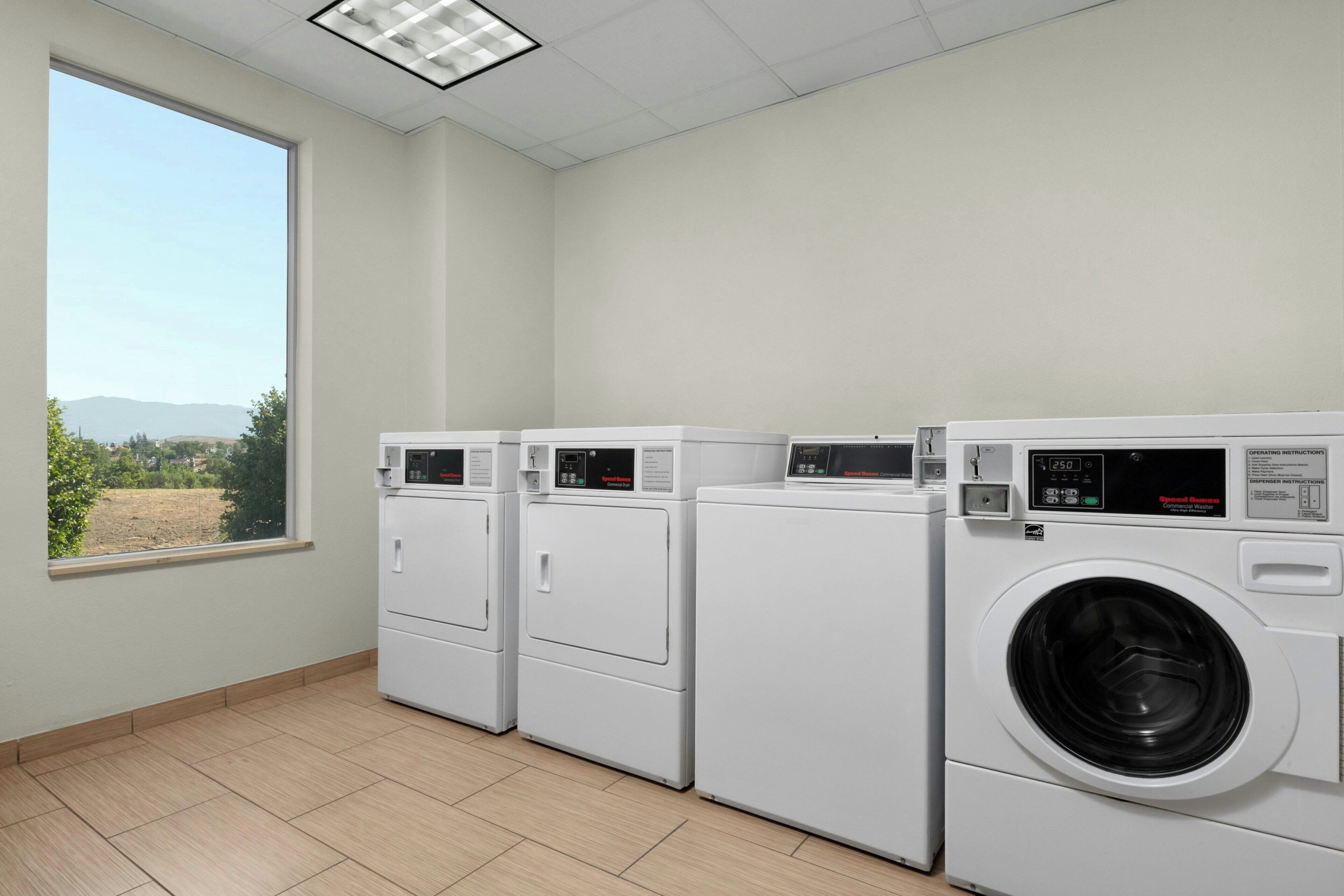 A laundry room with three stacked washers and dryers, a large window with a view of greenery and mountains, and a tiled floor.
