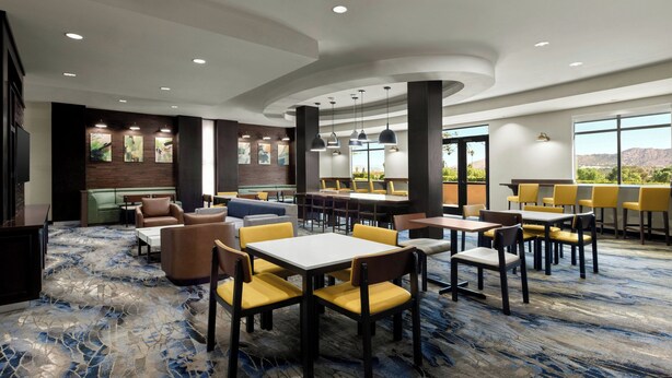 A modern hotel lobby with a mix of seating areas, including sofas and tables, and a bar area with yellow chairs. - Fairfield Inn & Suites Riverside Corona/Norco (Norco)