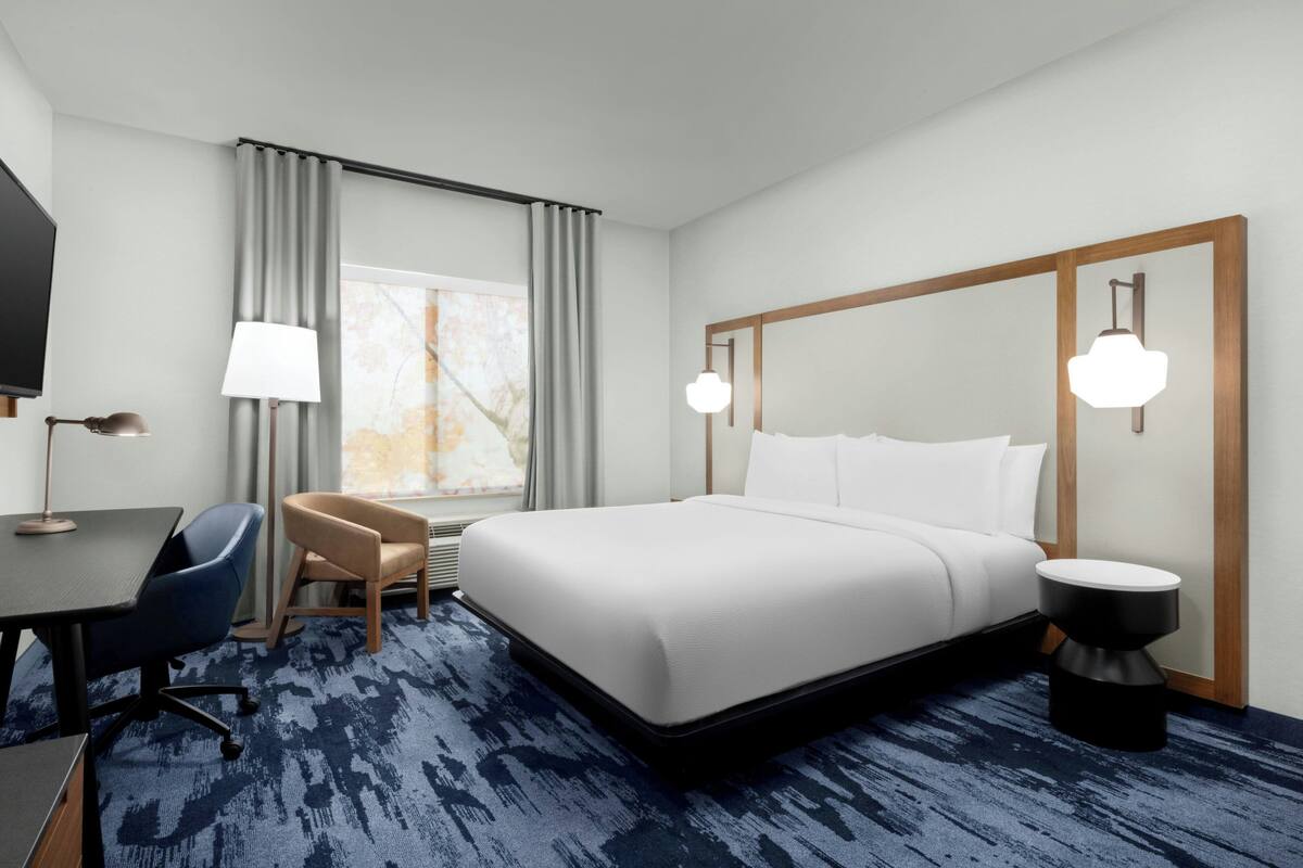 A hotel room with a large bed, a desk with a chair, a TV, and a window with curtains.