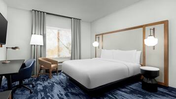 A hotel room with a large bed, a desk with a chair, a TV, and a window with curtains.