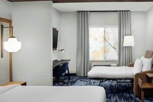 Habitación de hotel con cama, escritorio, silla, televisor y ventana con cortinas.