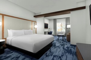 Habitación de hotel con una cama grande, un escritorio, una silla, un televisor y una ventana con cortinas.