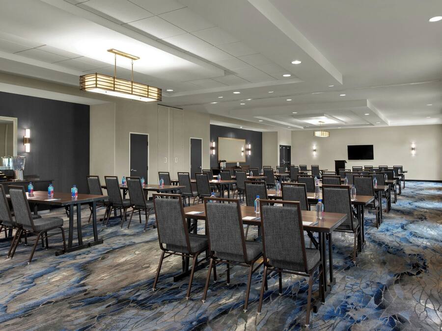 A conference room with multiple tables and chairs, a large mirror, and a flat-screen TV on the wall.