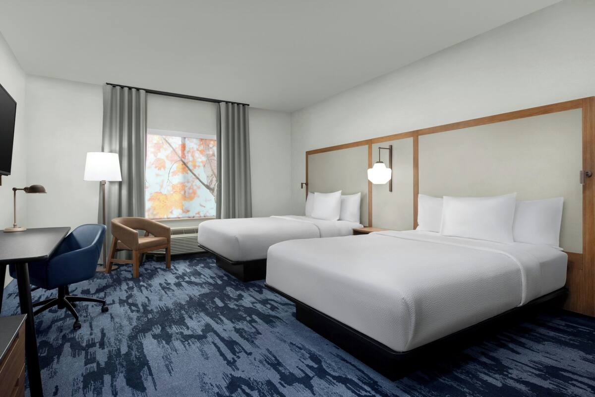 A hotel room with two beds, a desk, a chair, a TV, and a window with curtains.