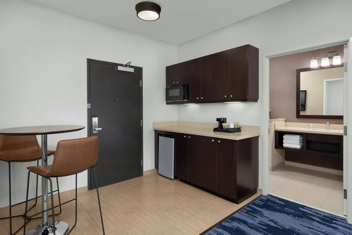 A compact kitchen with a microwave, dark cabinets, a small sink, and a dining area with two chairs.