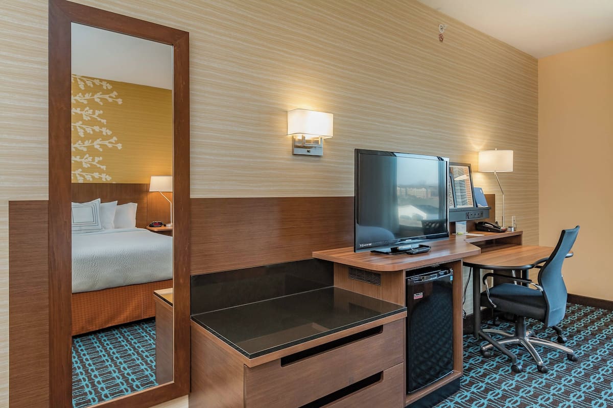 A hotel room with a bed, a desk with a computer, a chair, and a television.