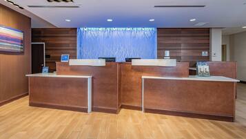 A reception area with wooden reception desks, a large digital screen, and a patterned wall.