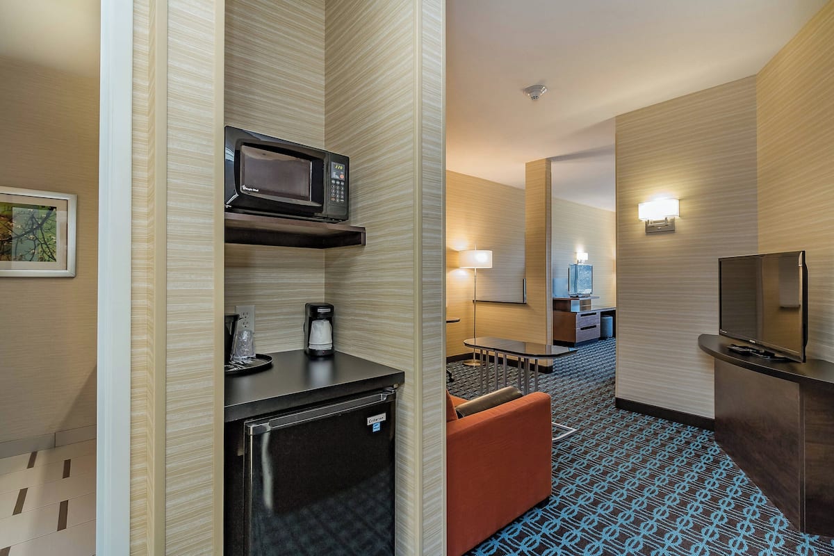 A hotel room with a kitchenette, a TV, a sofa, a small table, and a lamp.