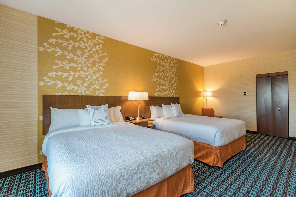 A hotel room with two beds, a wooden headboard, a patterned carpet, and a door.