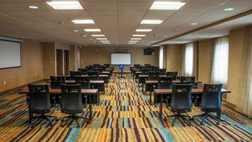 A conference room with rows of tables and chairs, a projector screen, and a carpeted floor.