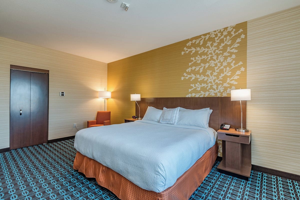 A hotel room with a large bed, two bedside tables with lamps, a wooden headboard, and a patterned carpet.