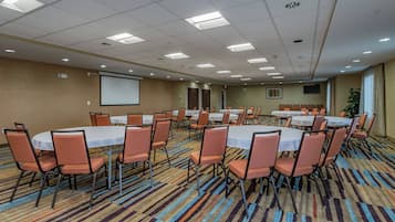 Un salón de conferencias con varias mesas y sillas, una pantalla de proyector y suelo alfombrado.