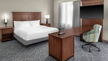 A hotel room with a bed, bedside tables, a desk, a chair, and a flat-screen TV.