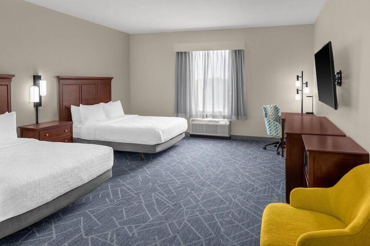 A hotel room with two beds, a desk, a chair, a TV, and a window with curtains.