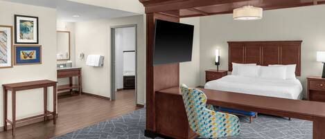 Habitación de hotel con cama, escritorio, silla, televisor y baño visible a través de una puerta abierta.