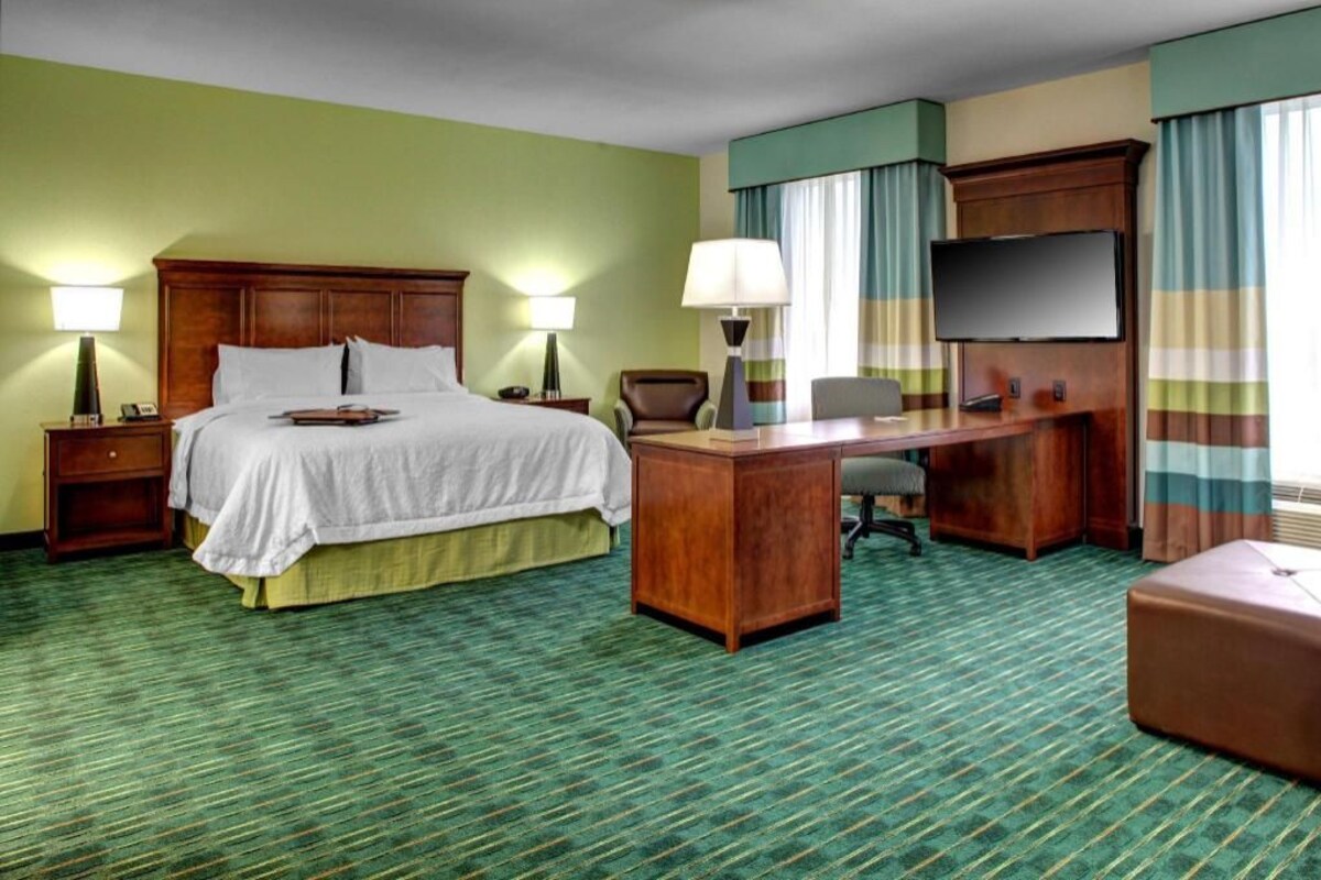 A hotel room with a bed, desk, chair, TV, and curtains.