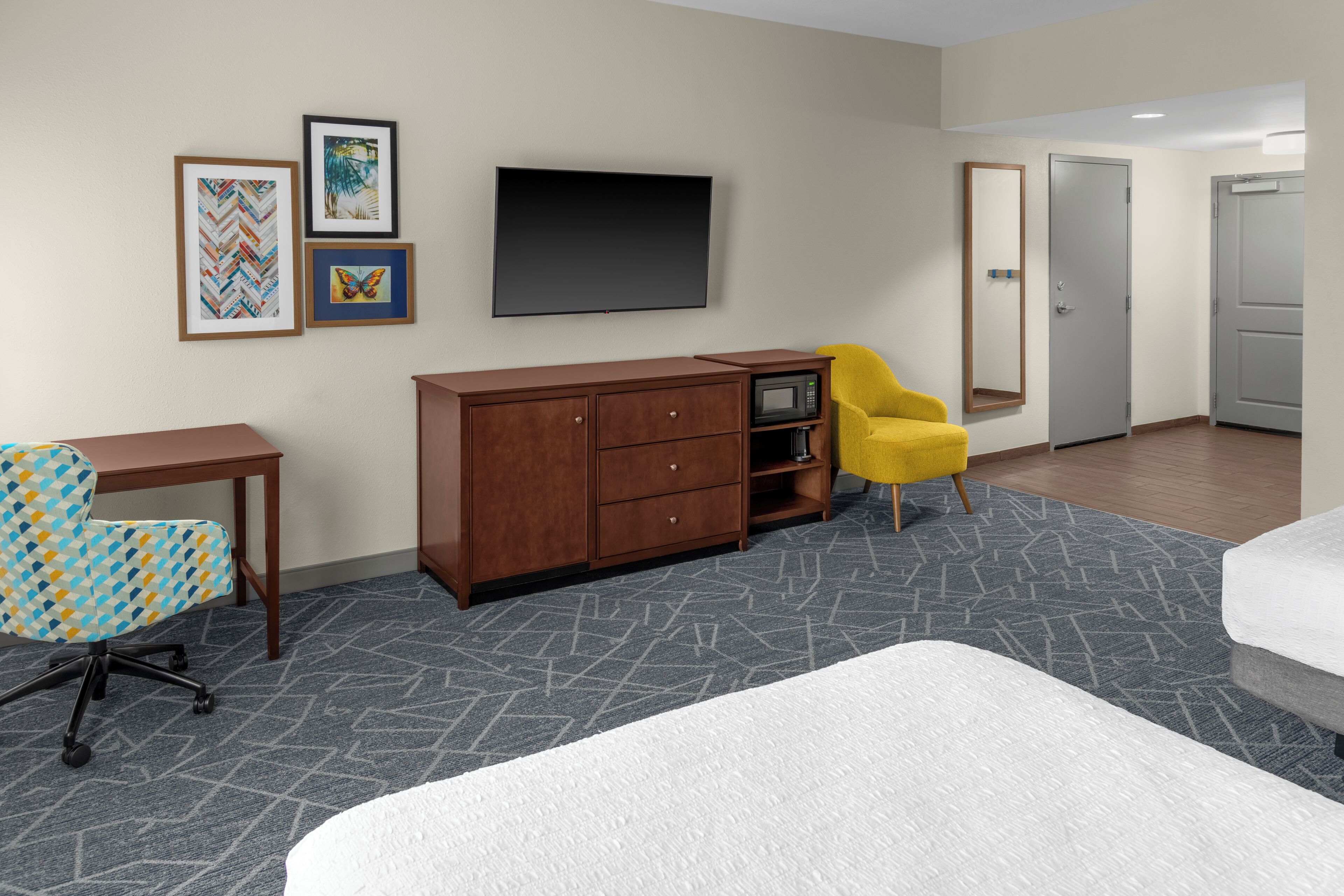 A hotel room with a bed, a desk, a chair, a wardrobe, a television, and artwork on the wall.