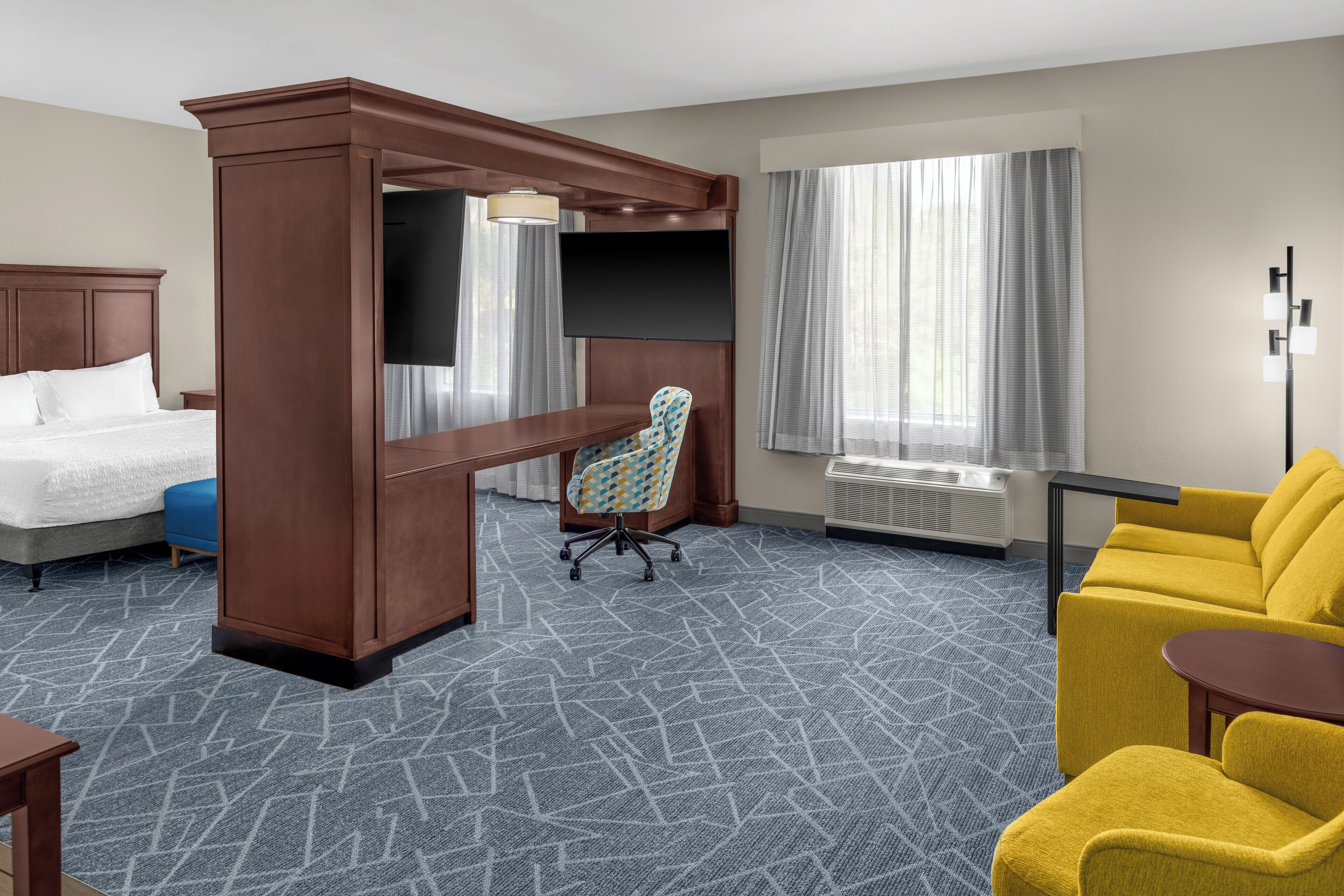 Ein Hotelzimmer mit einem Bett, einem Schreibtisch mit Stuhl, einer Couch und einem Fernseher.
