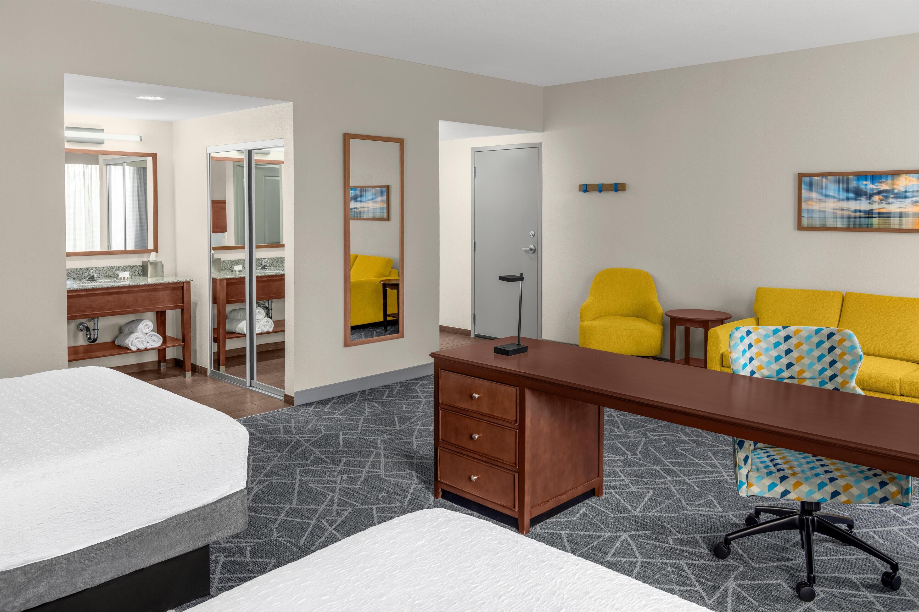 Une chambre d’hôtel comprenant un lit, un bureau, une chaise, un canapé, une salle de bain avec un miroir et une porte.
