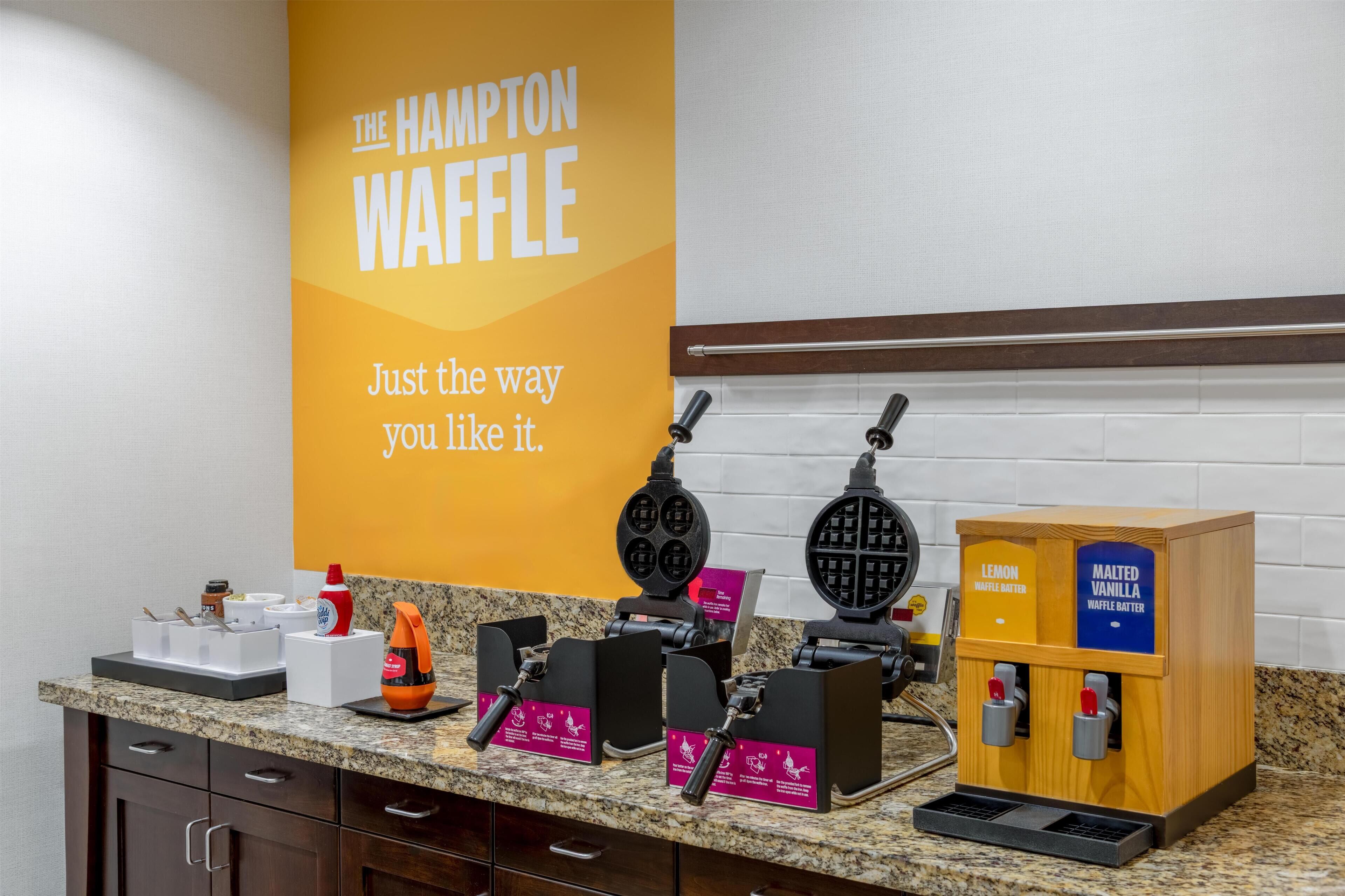 A kitchen counter with waffle makers, a waffle batter station, and a sign that reads "The Hampton Waffle".
