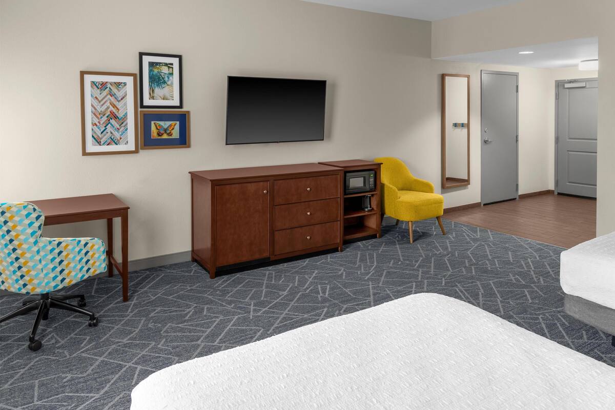 A hotel room with a bed, a desk, a chair, a wardrobe, and a flat-screen TV.