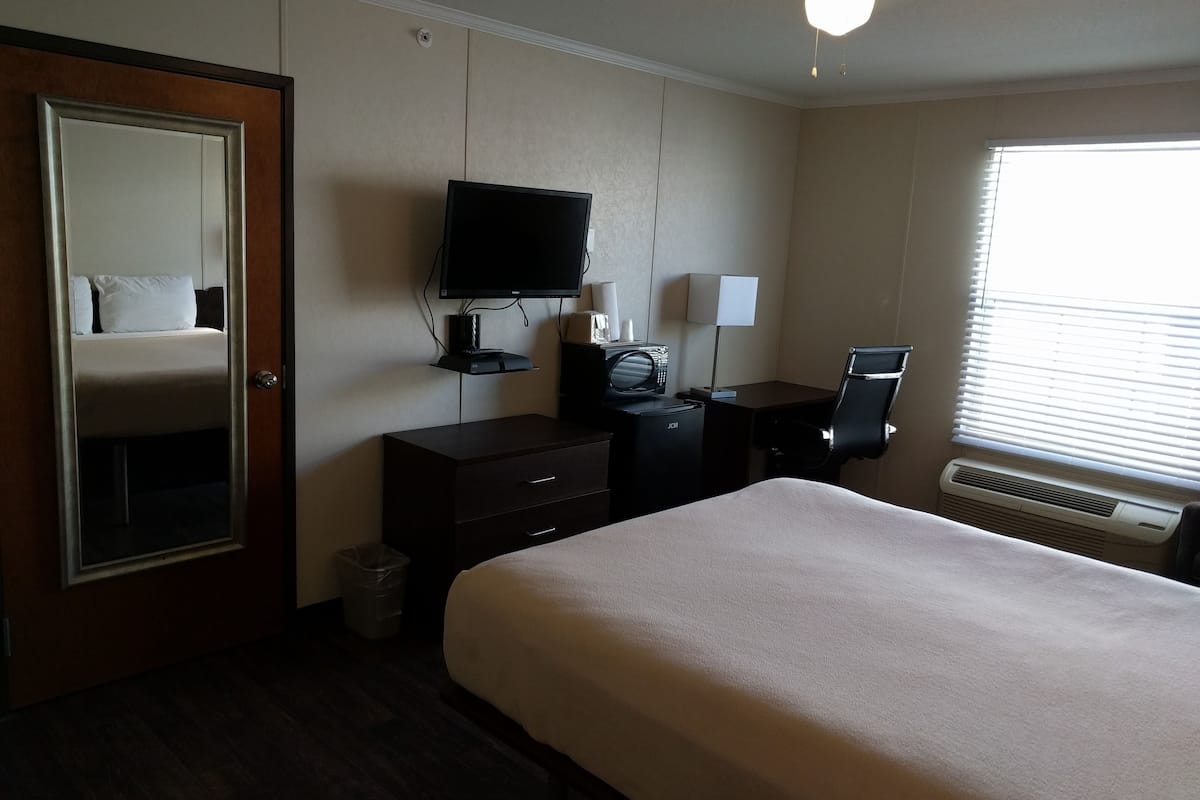 Ett hotellrum med en säng, ett skrivbord med en dator, en tv och ett fönster med persienner.