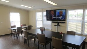 A conference room with a large table, six chairs, and a television screen displaying a news program.