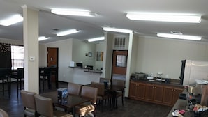 A spacious dining area with multiple tables and chairs, a kitchen area with appliances, and a reception desk.