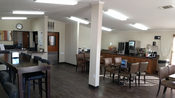 A spacious room with a long wooden table and chairs, a kitchenette area, and a clock on the wall.