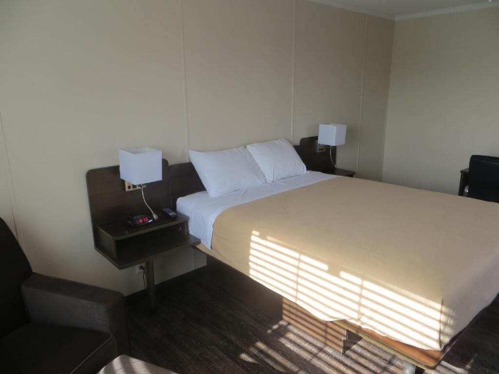 A hotel room with a large bed, two bedside tables, a chair, and a desk.
