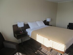 A hotel room with a large bed, two bedside tables, a chair, and a desk.