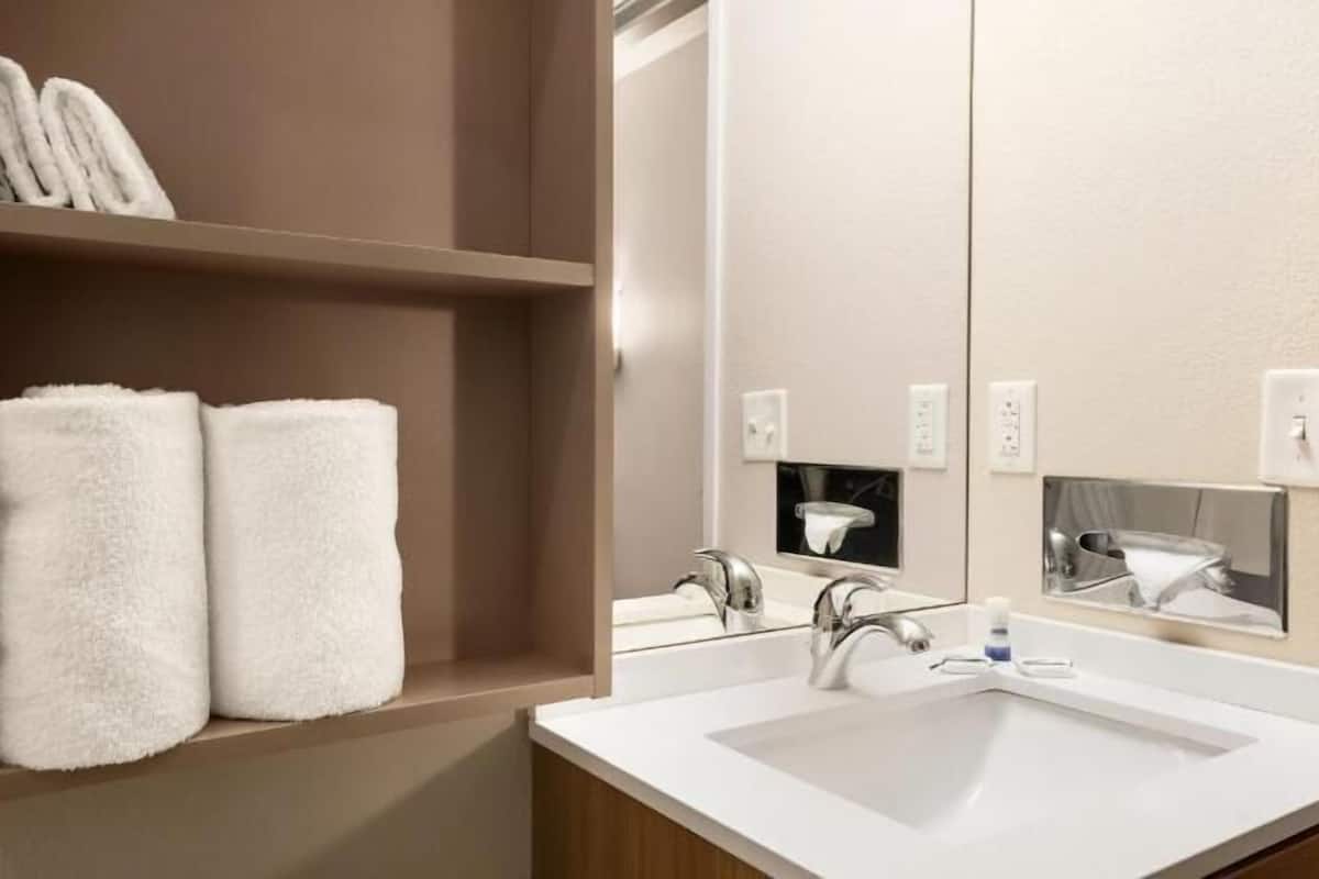 Une salle de bain avec un lavabo blanc, un miroir et une étagère sur laquelle reposent deux serviettes pliées.