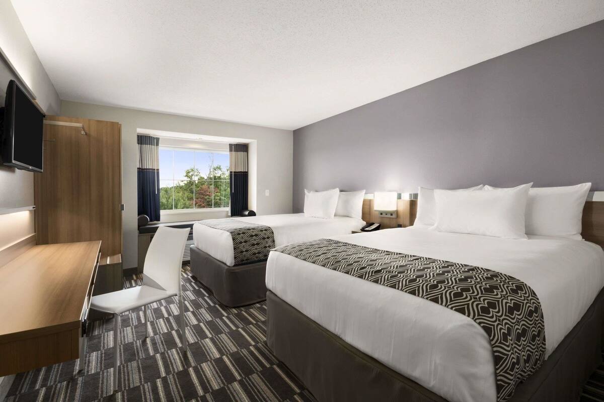 Une chambre d’hôtel avec deux lits, un bureau, une chaise, une télévision et une fenêtre avec des rideaux.