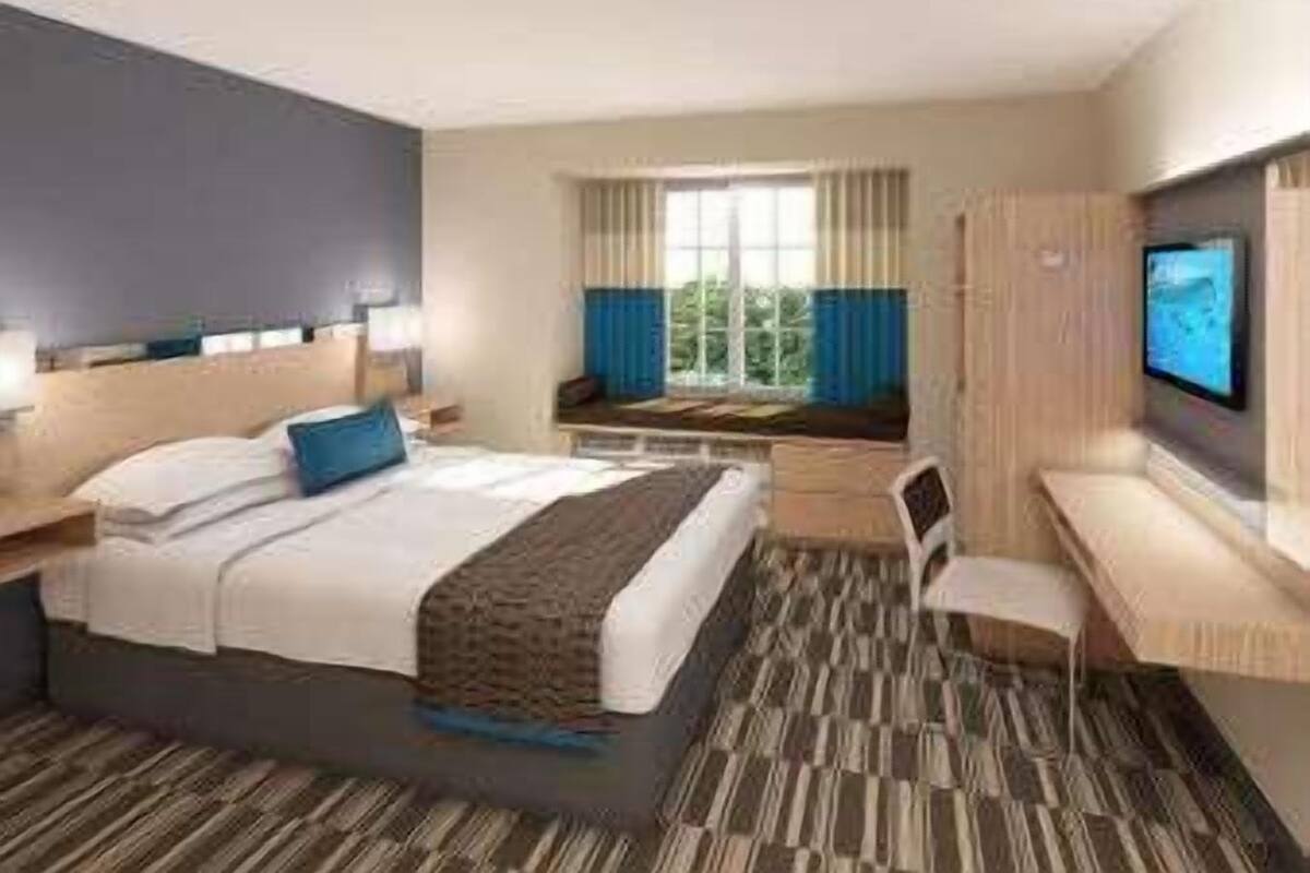 Une chambre d’hôtel avec un lit, un bureau, une chaise, une télévision et une fenêtre avec des rideaux.