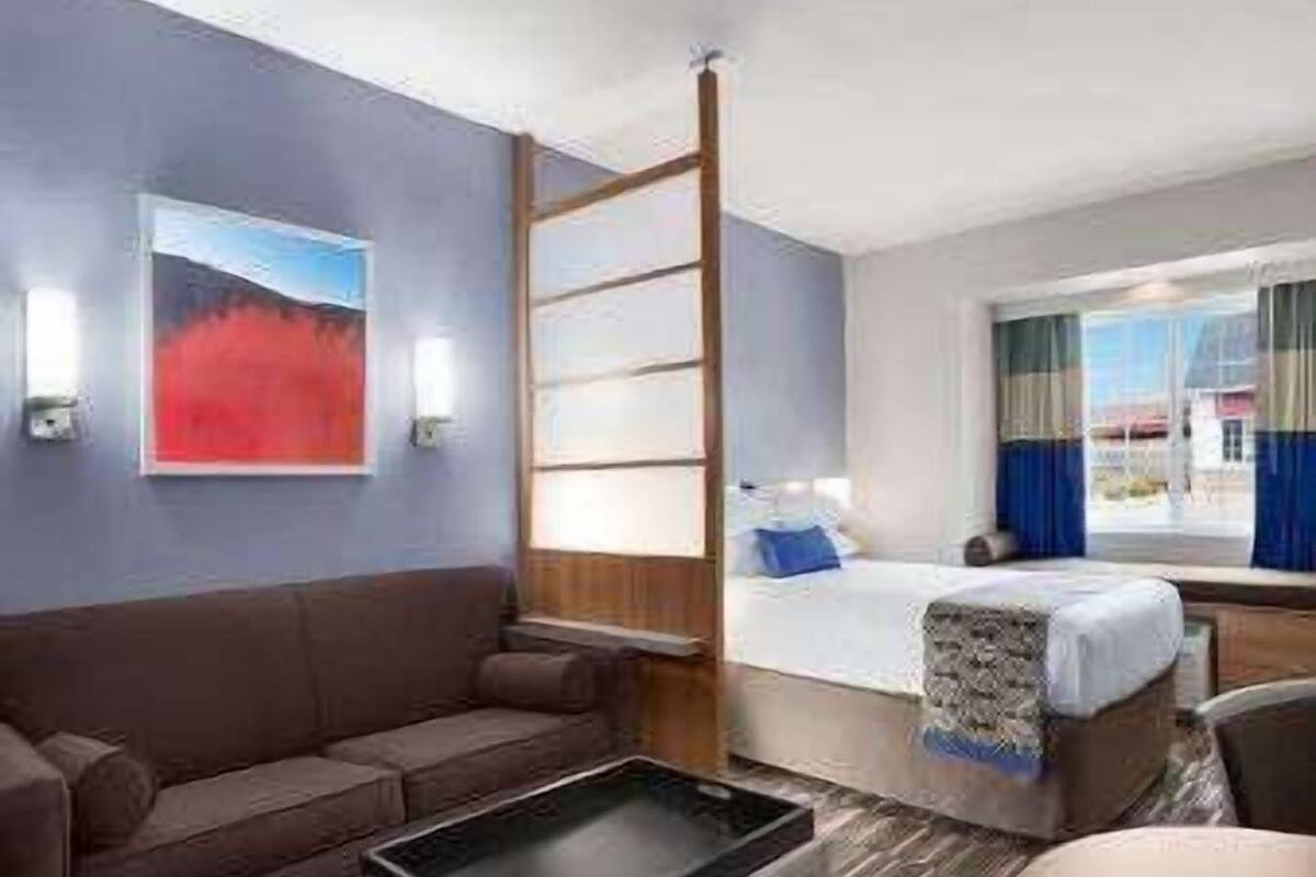 Une chambre d’hôtel avec un lit, un canapé, un bureau, une fenêtre avec des rideaux et un tableau au mur.