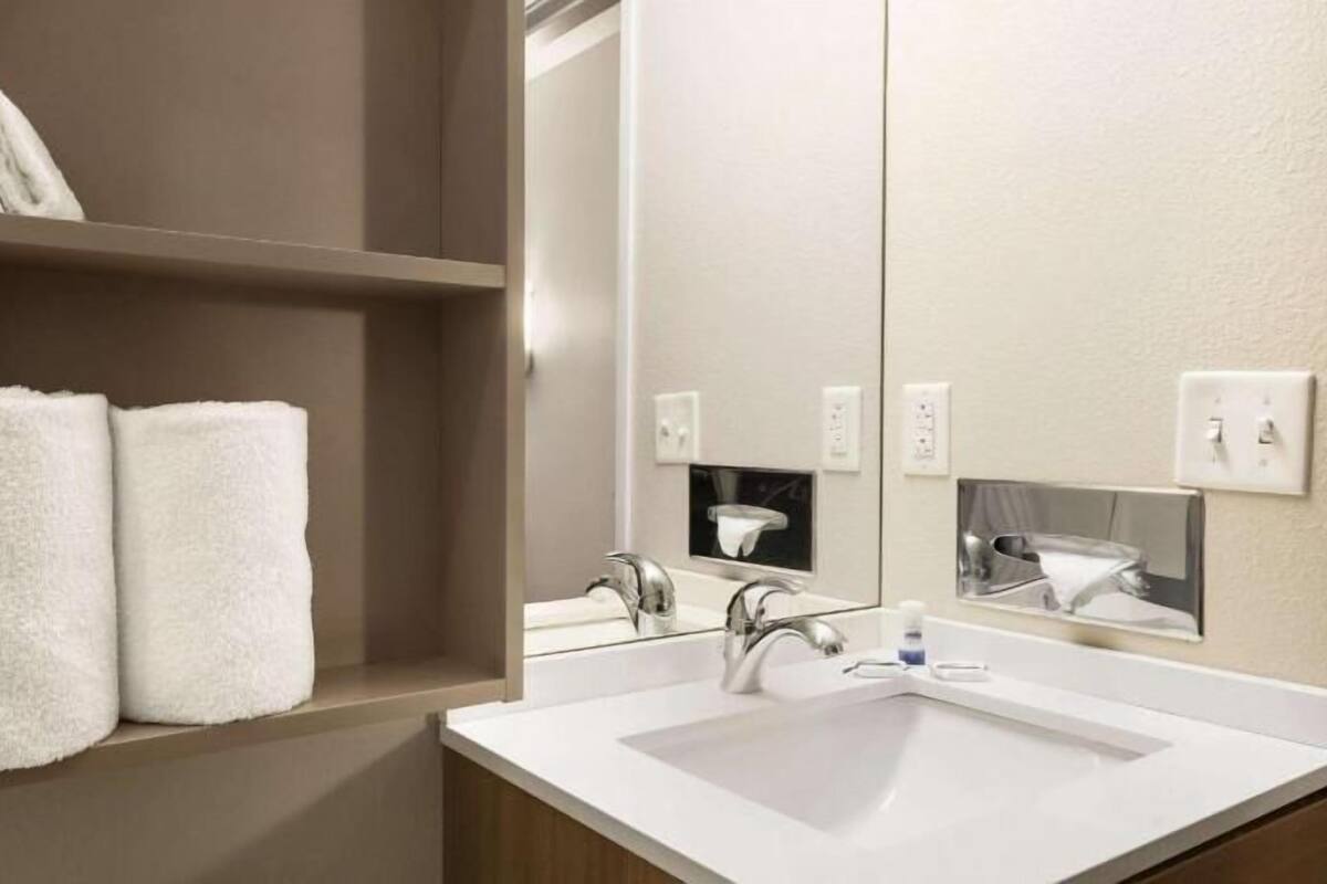 Une salle de bain avec un lavabo blanc, un miroir et deux serviettes blanches posées sur une étagère.