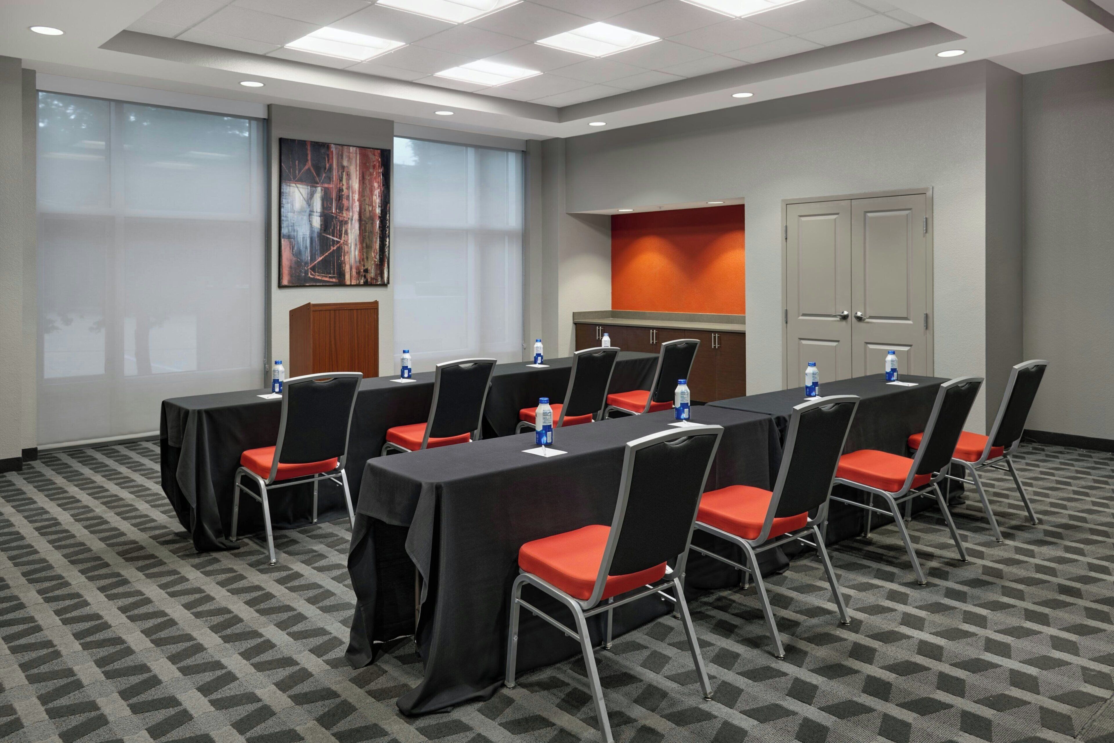 A conference room with a long table, chairs, water bottles, and a projector screen.