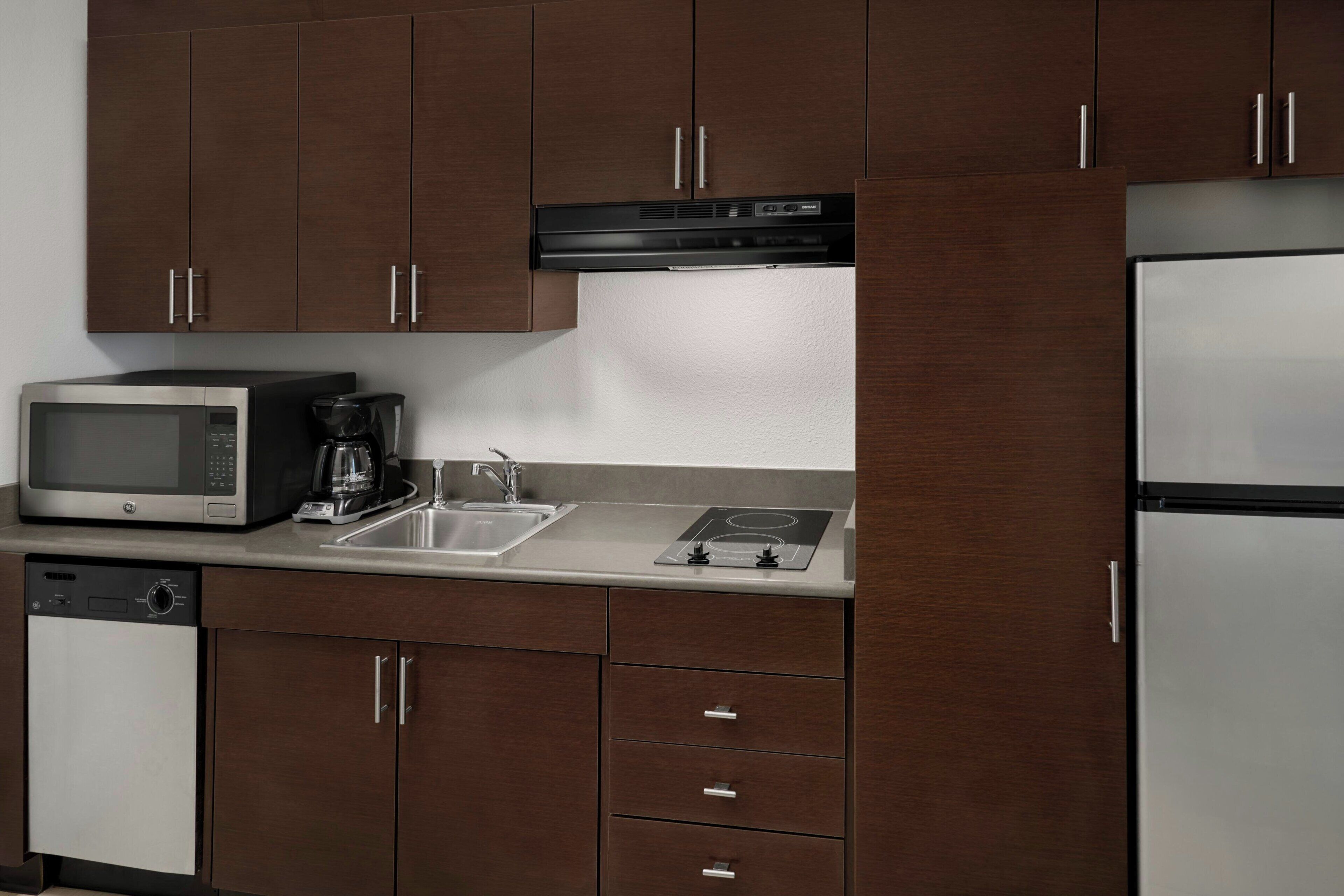Una cocina con armarios de madera oscura, un refrigerador de acero inoxidable, un microondas, una cafetera y un lavavajillas.