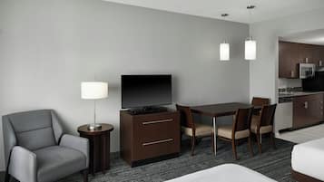 Habitación de hotel con cama, escritorio con televisor, silla, lámpara y kitchenette.